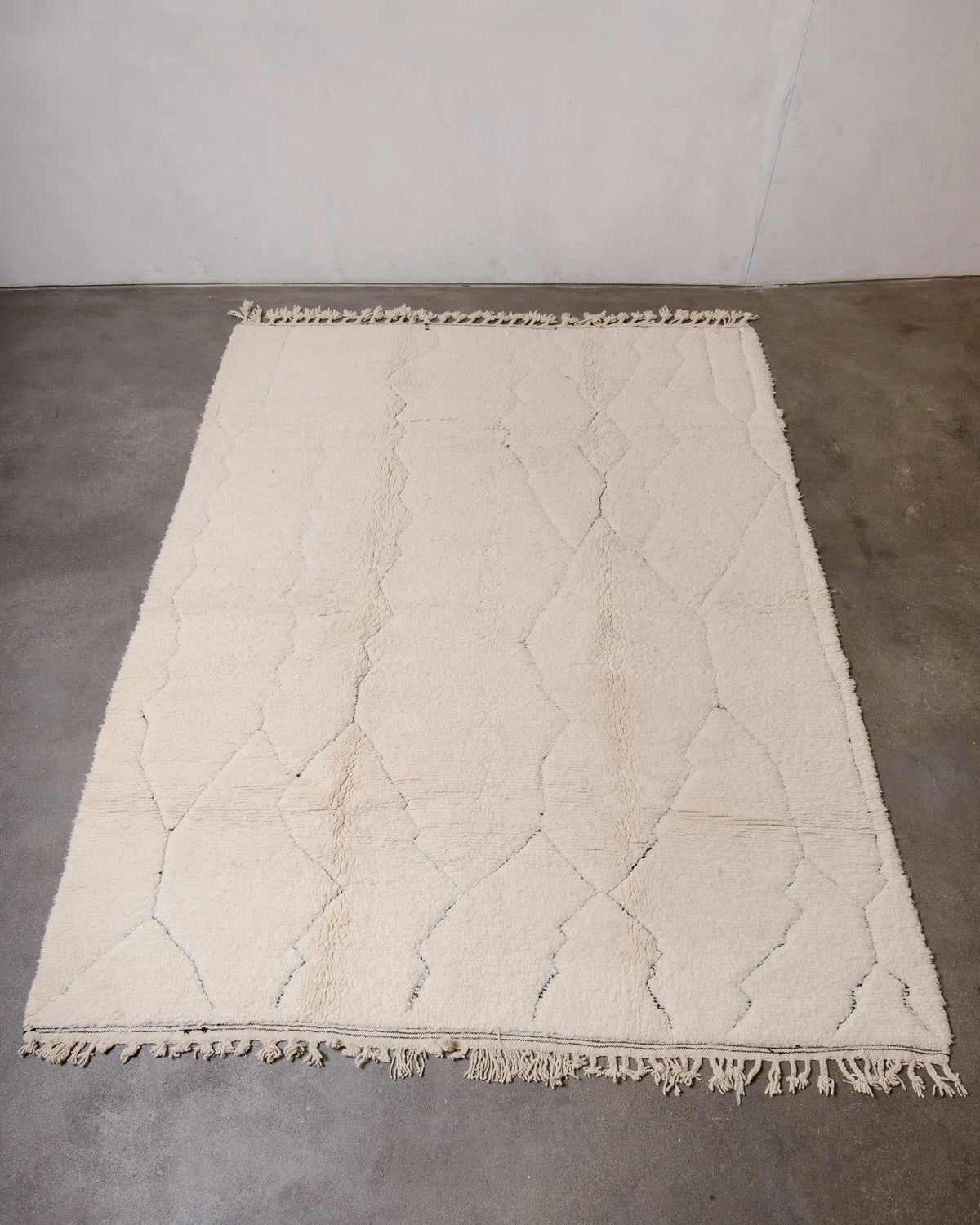 Berberlin Beniourain Rug made of cream wool with a subtle, abstract woven design in black, photographed on a concrete studio floor.